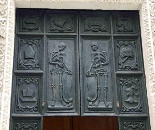 Carvings on the huge  wooden door depict mirror-image skeletons surrounded by the trappings of kings and cardinals