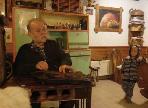 His grandad, Ivan, plays an alpine zither that was once owned by Ivan's father; now Ivan is teaching his grandson to play (the plectrum he's using was carved from goat horn)